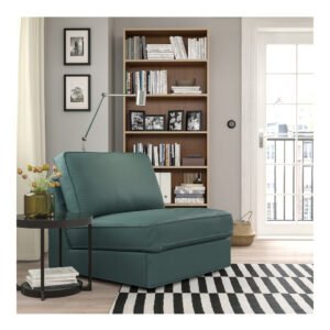 A cozy living room corner with a green armchair, a side table, a bookshelf, and framed artwork on the walls.