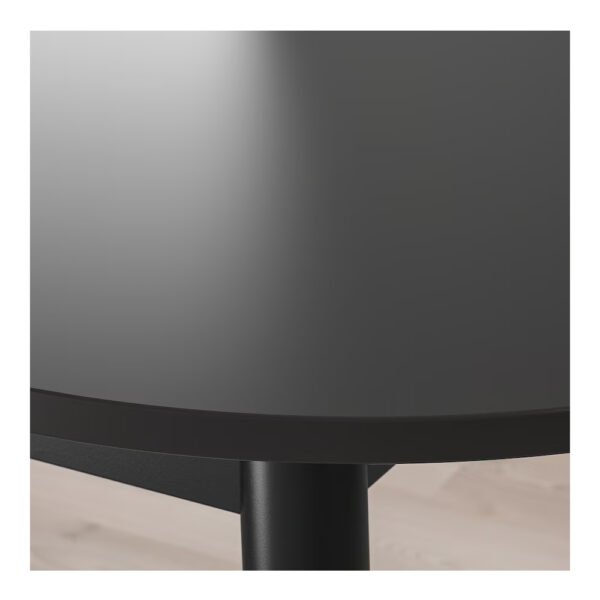 Close-up view of the black, circular tabletop and metal leg of a modern dining table.